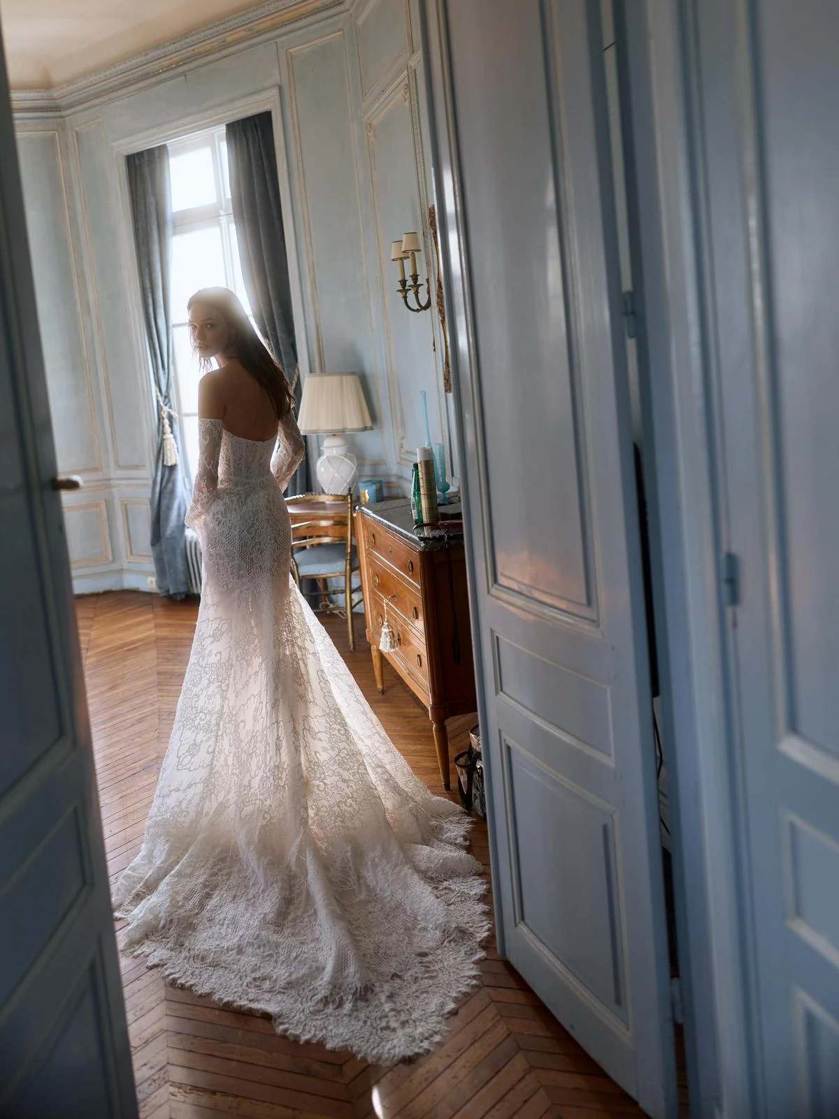 Abito da sposa visto di schiena in una stanza dai toni azzurri. — selezione Maison Yana, riferimento 011