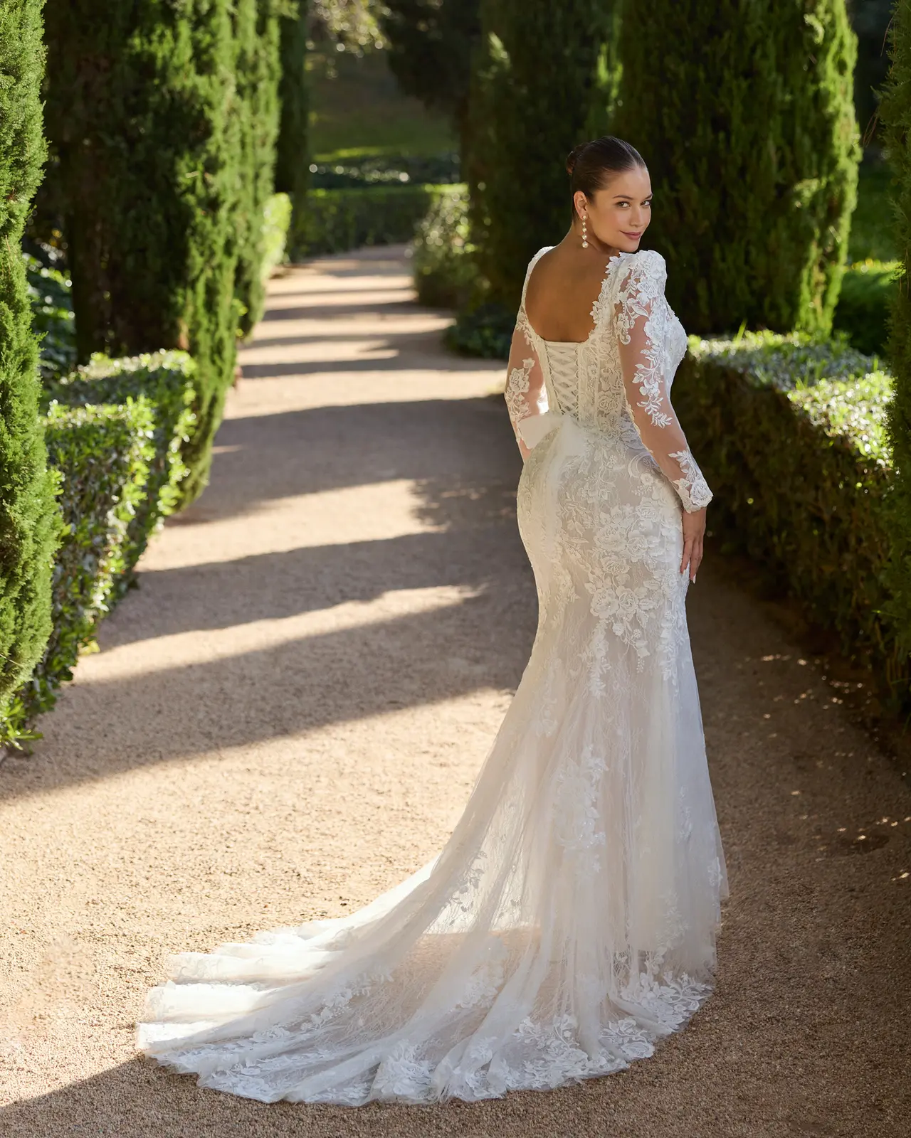 Vista posteriore di un abito da sposa aderente, con maniche trasparenti decorate, scollatura sulla schiena e strascico.