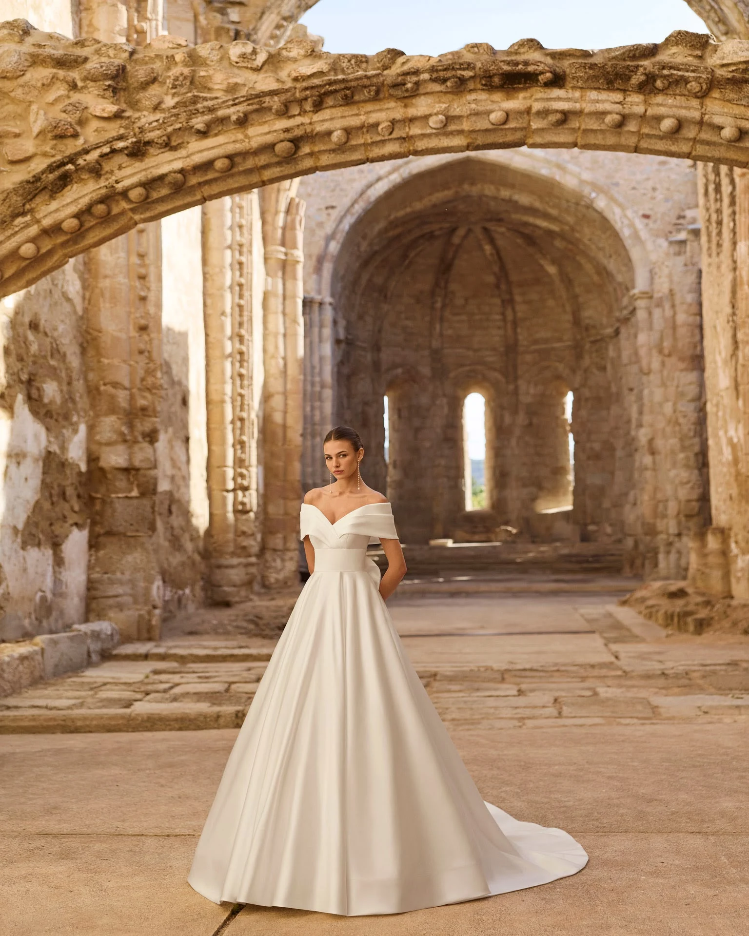 Abito da sposa AIRE Atelier: scollo omerale e gonna ampia tra gli archi