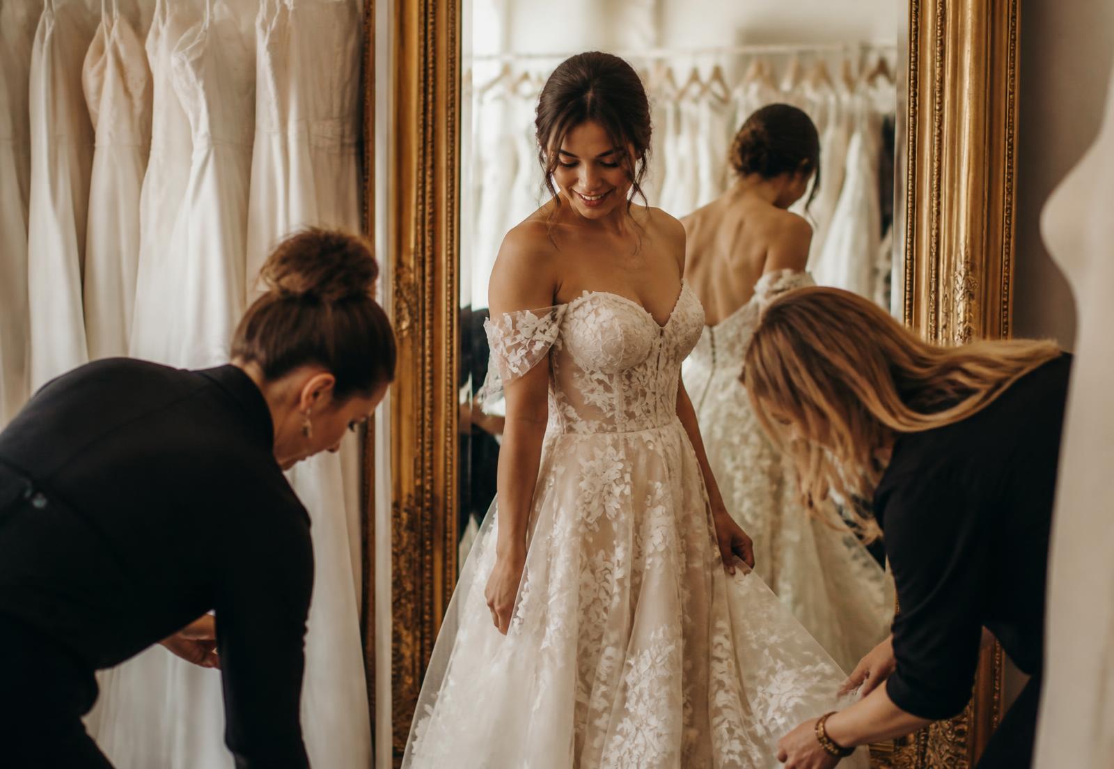 Sposa alla prova dell'abito davanti allo specchio con le consulenti dell'atelier